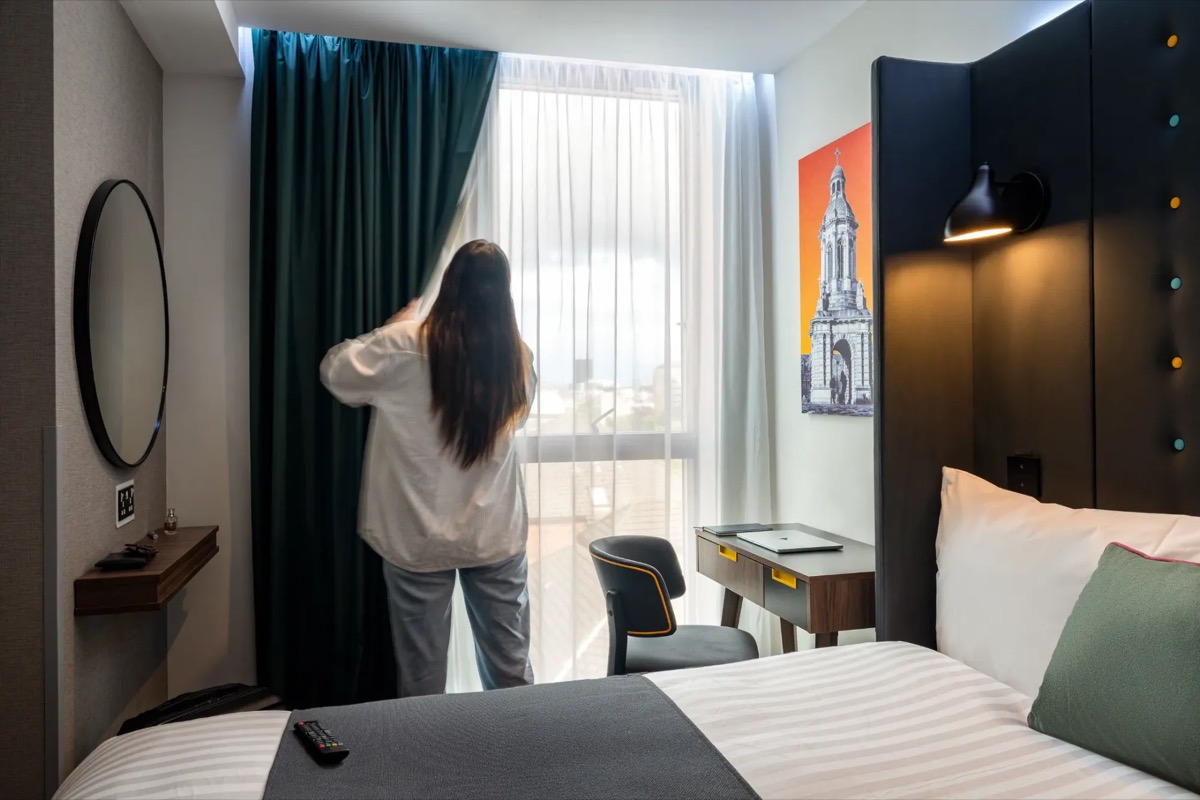 A guest opening the curtains in a Point A Hotels room