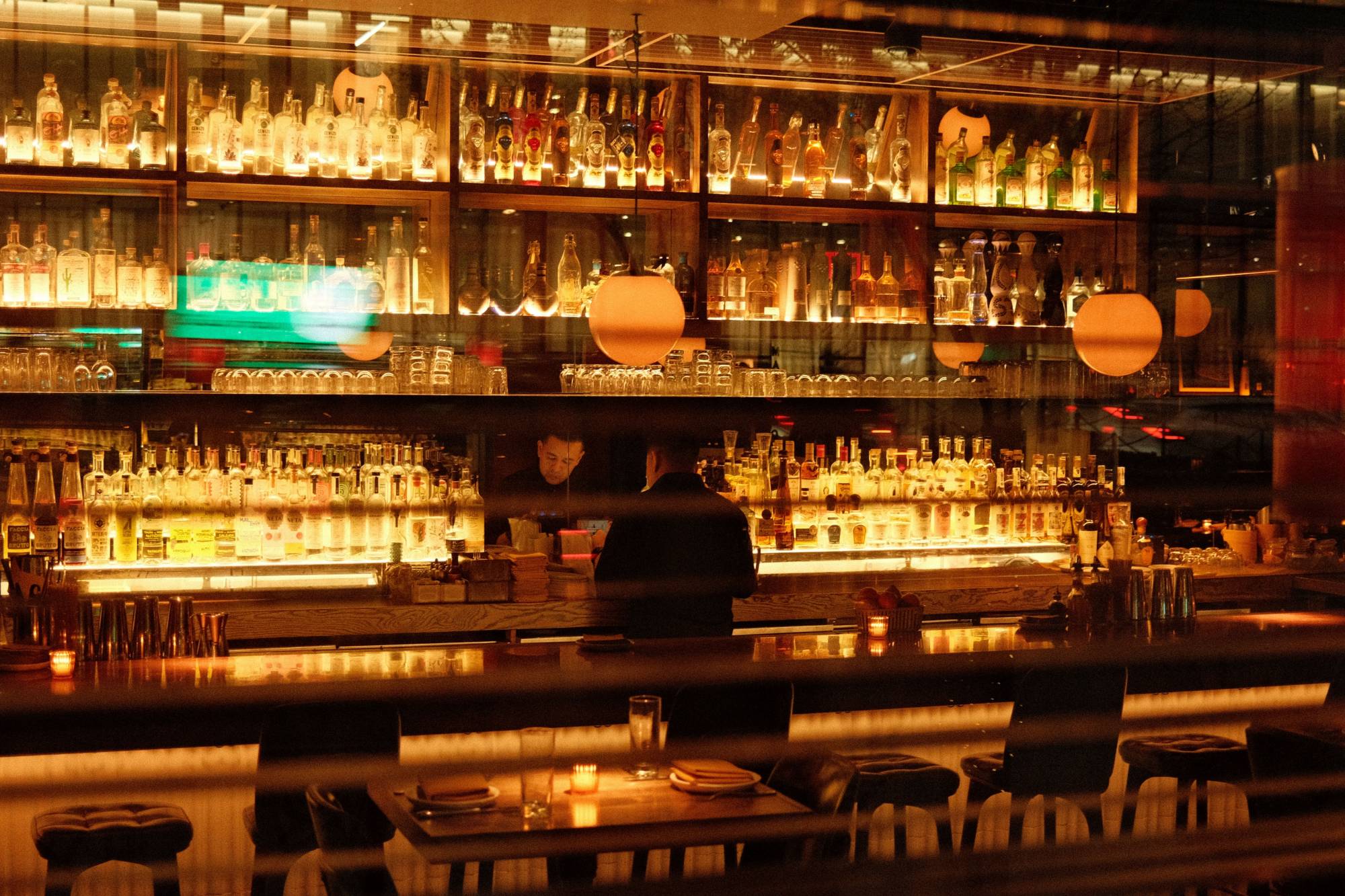A candlelit cocktail bar with backlit shelves of bottles