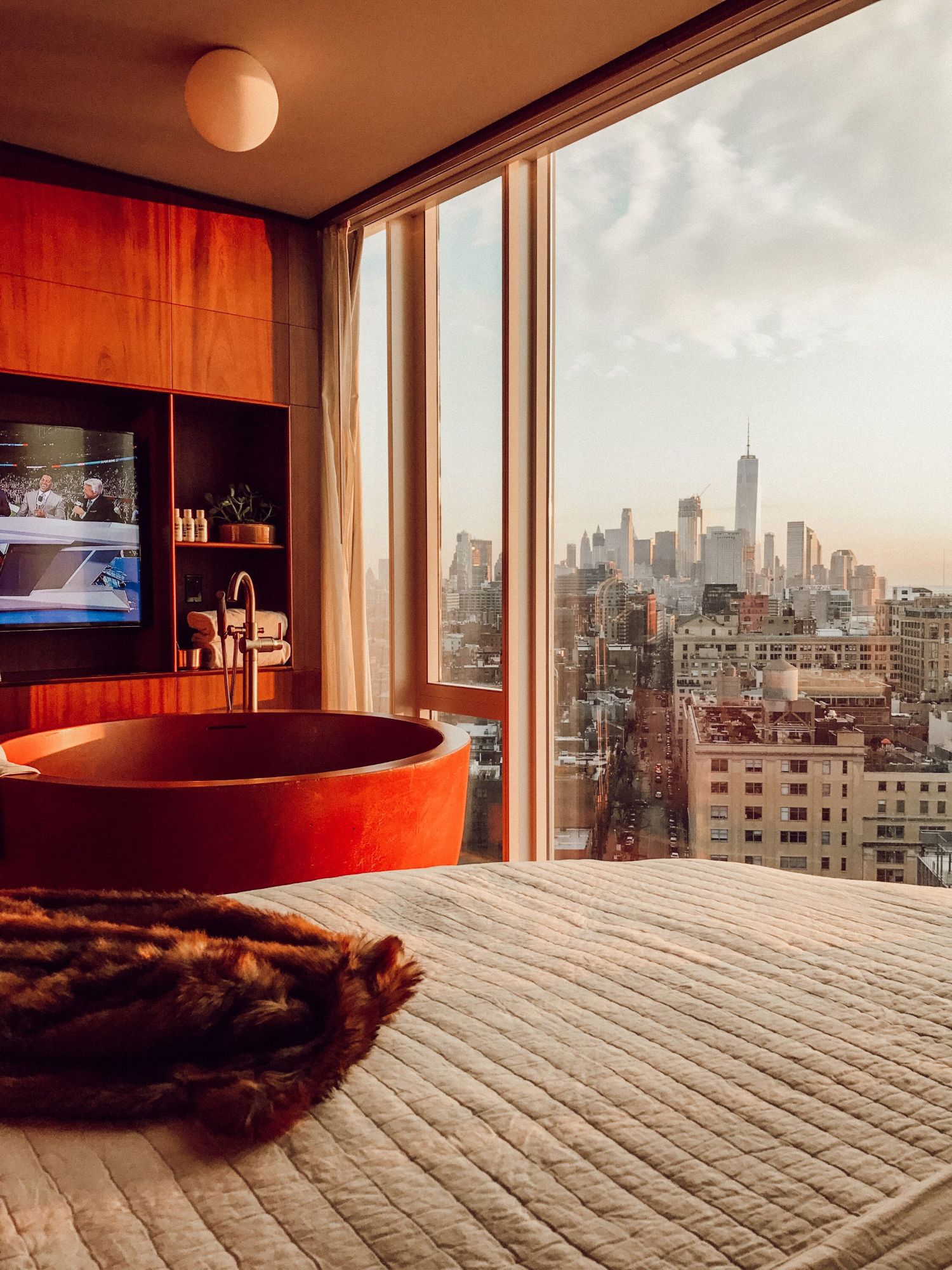 A hotel room with a freestanding bath and floor-to-ceiling windows looking out over Manhattan