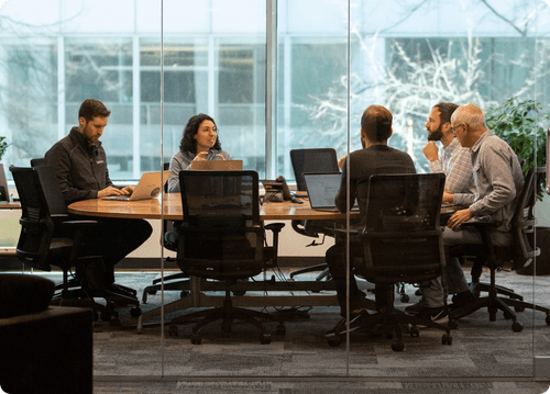 A group of Galois employees sitting around a wooden table in a glass conference room.
