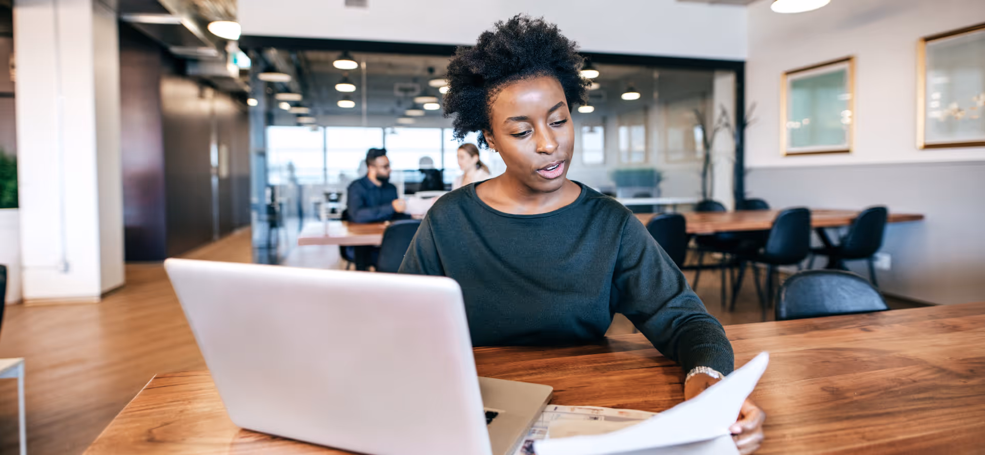 Businesswoman reviewing documents while working on a laptop in a modern office.