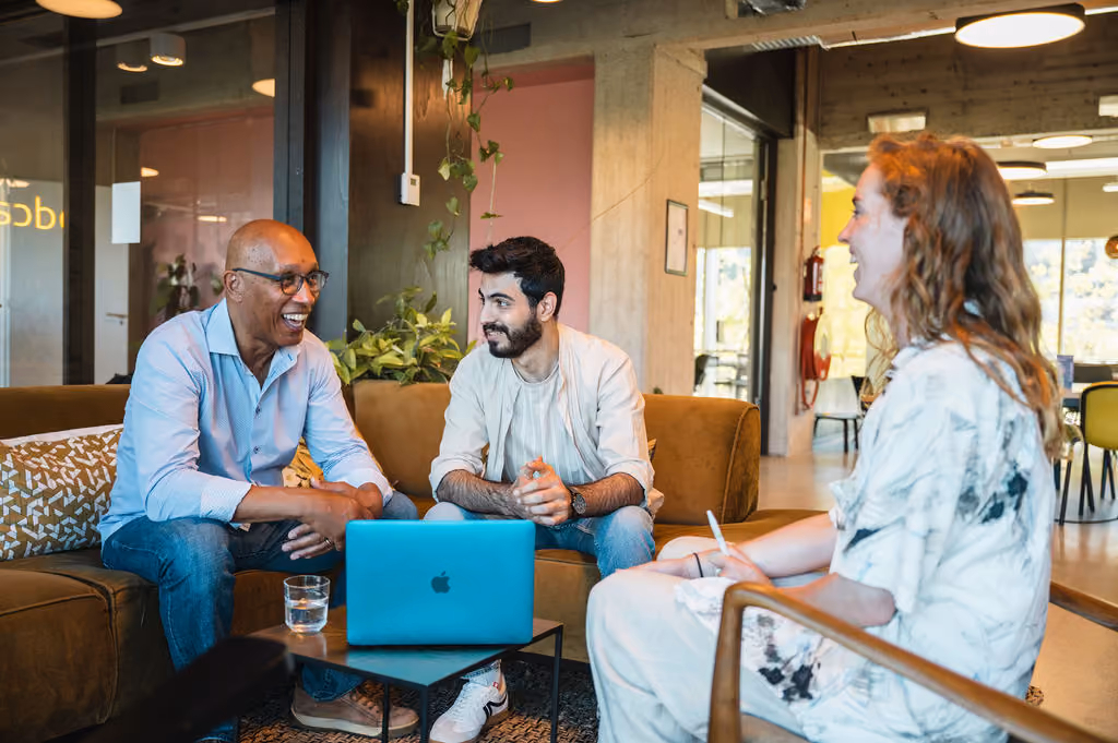 Een coördinator van DUO for a JOB legt aan een duo, een jonge zwarte man en een blanke man boven de 50, een hulpmiddel uit voor het zoeken naar een baan.