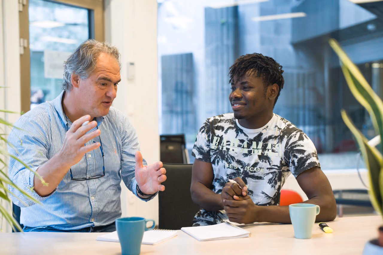 A man over 60 is talking to a young man of African origin in one of the DUO for a JOB antennas, the young man smiles
