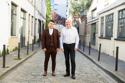 Un senior et un jeune homme en blazer bleu marine sont debout dans la rue et sourient en regardant le photographe