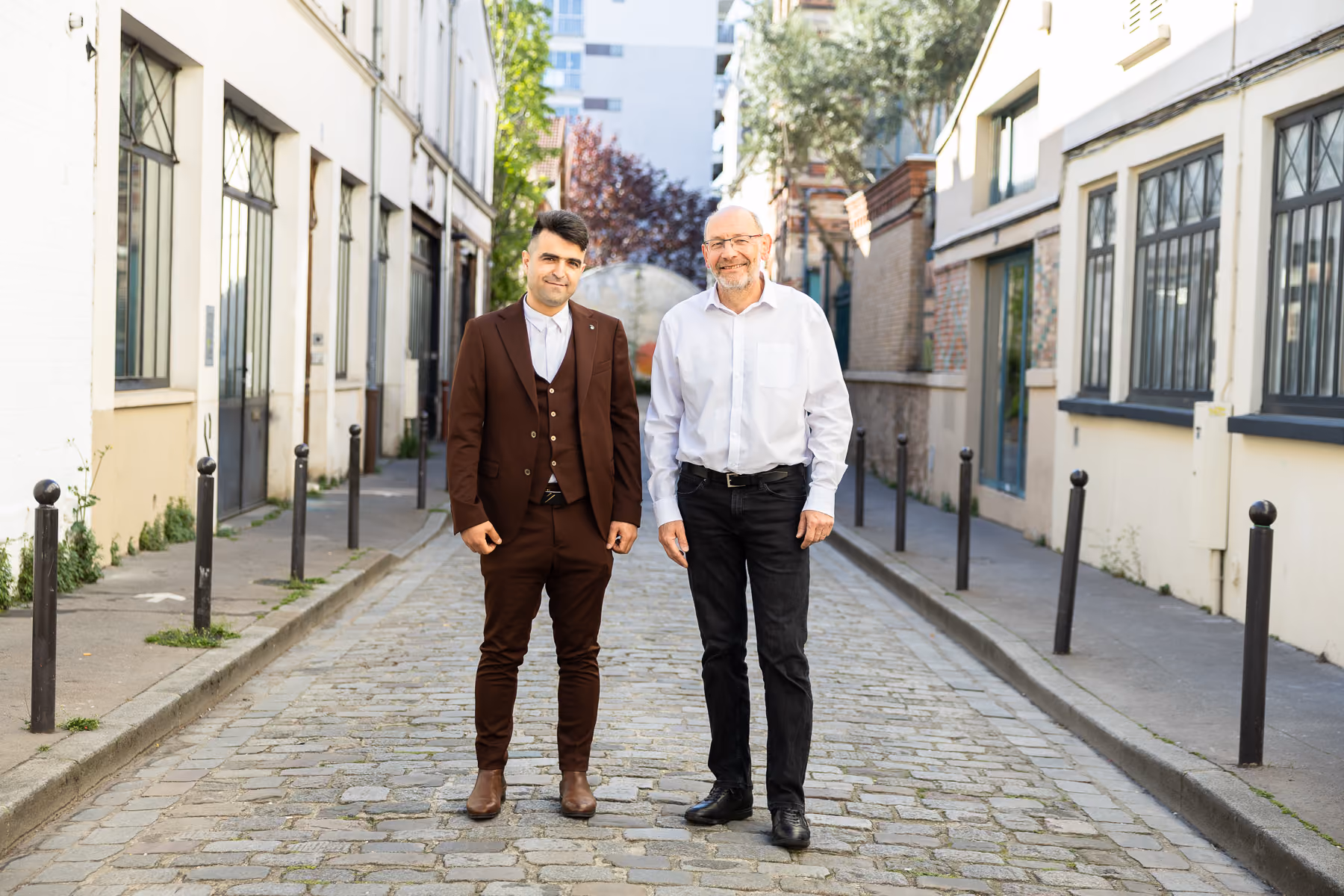 Un senior et un jeune homme en blazer bleu marine sont debout dans la rue et sourient en regardant le photographe