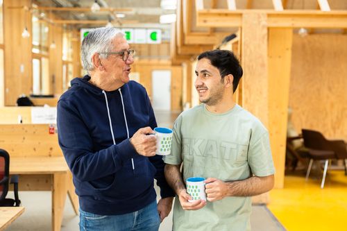 une jeune femme noire dans une robe bleue et noire est assises auprès de sa future mentor sur des chaises noires dans un patio entourée de plantes. Elles discutent ensemble.