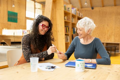 Un jeune homme noir sourit timidement aux côtés de sa mentor une femme de 50 ans avec les cheveux roux