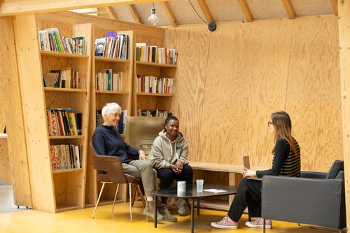 Un homme de plus de 50 ans avec des lunettes et une chemise blanche est assis à une table avec une jeune femme avec de longs cheveux noirs. Ils ont de quoi écrire et un ordinateur sur la table devant eux.
