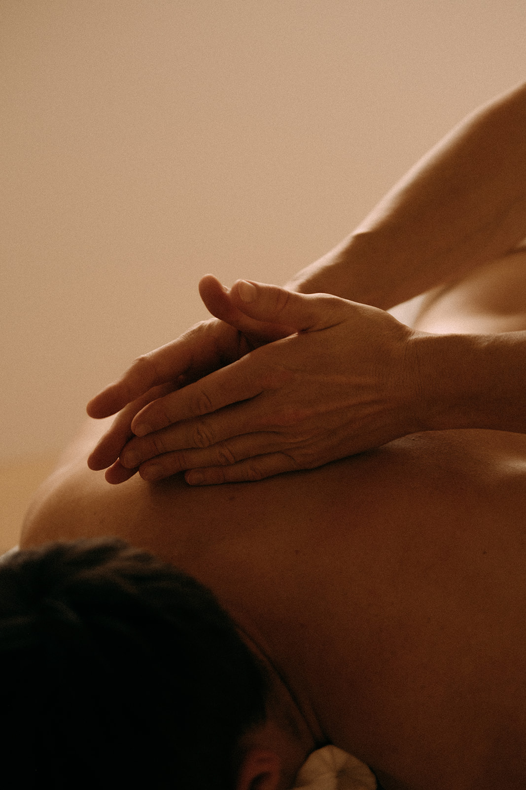 Ein Mann liegt auf dem Bauch auf einer Massageliege. Zwei Hände massieren den oberen Rücken des Mannes.