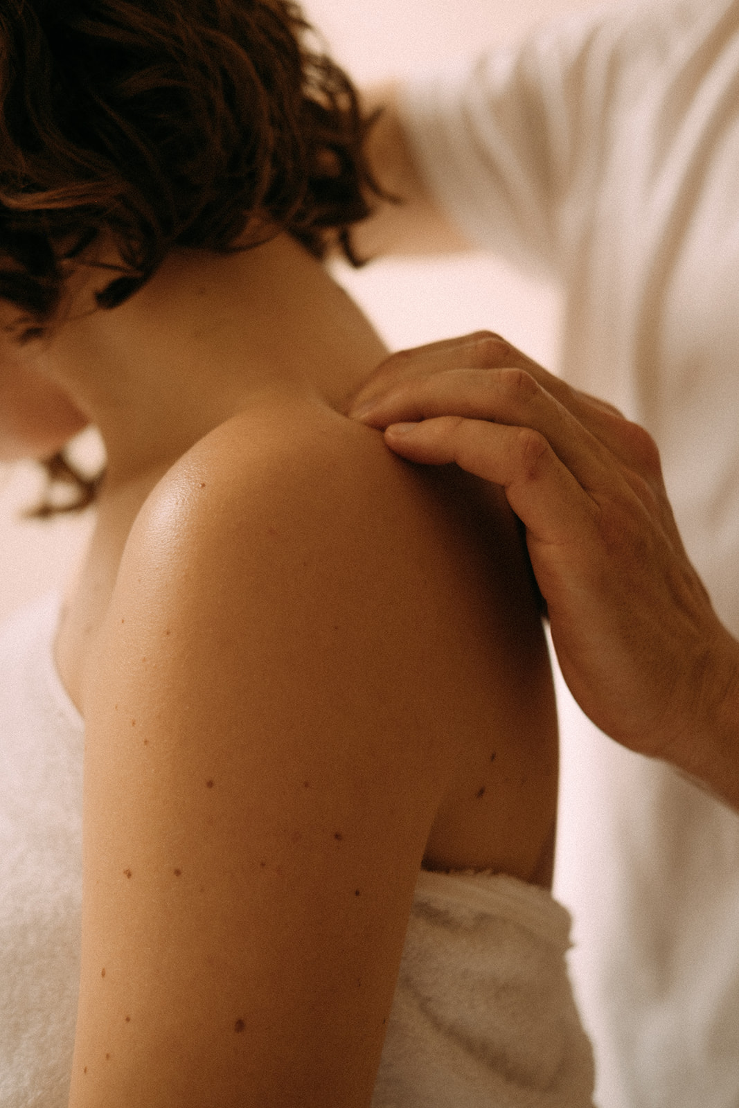Eine Frau sitzt auf einer Massageliege. Sie wird an den Schultern und am Nacken massiert.