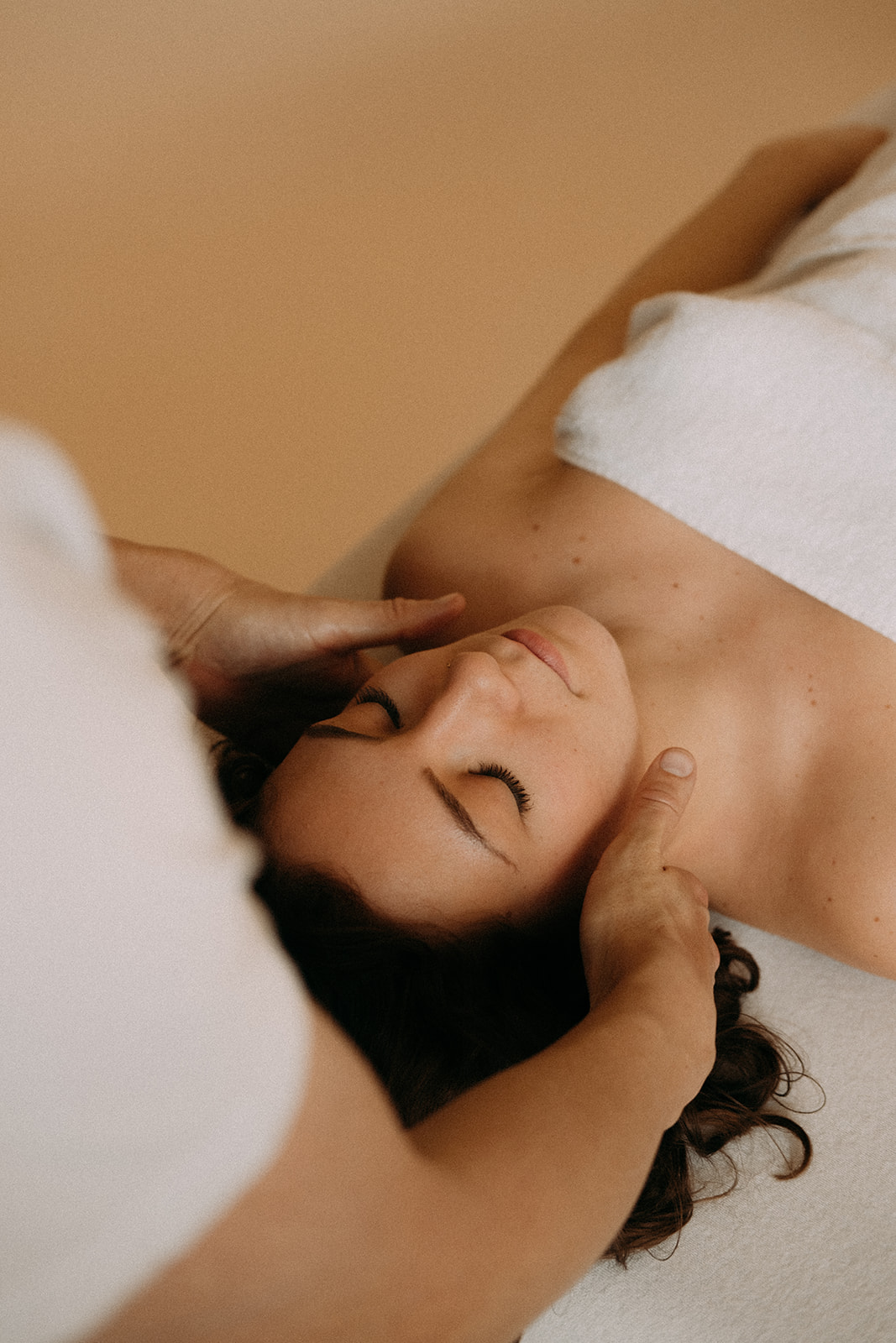 Eine Frau liegt auf der Rücken auf einer Massageliege. Sie hat die Augen geschlossen. Sie wird am Kopf und Nacken von einem Masseur massiert. 