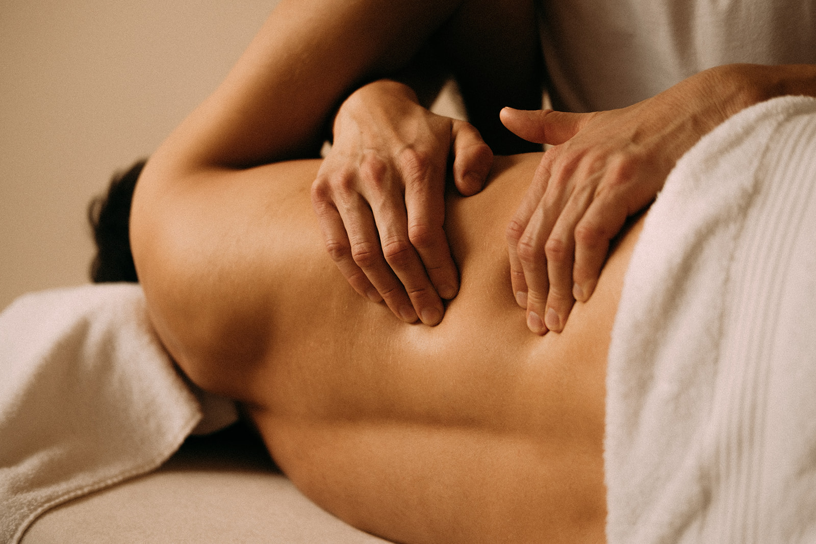 Ein Mann liegt seitlich auf einer Massageliege. Er wird am seitlichen Oberkörper massiert. Im Fokus sind die Hände, die den seitlichen Oberkörper massieren.