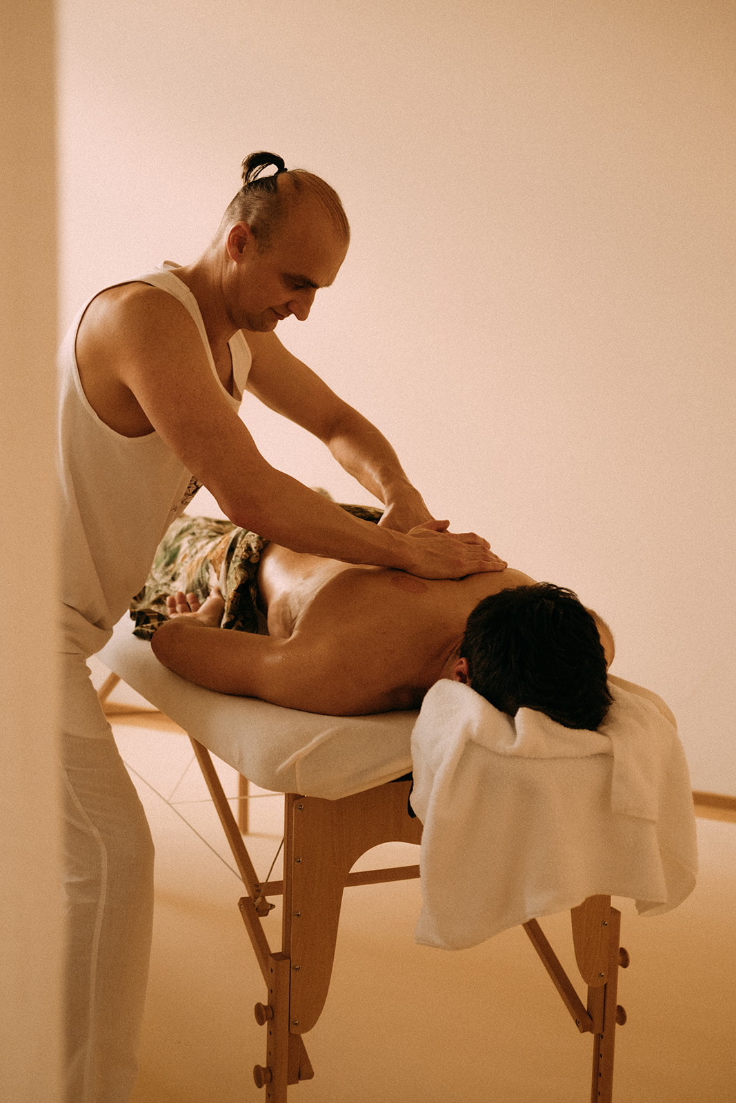 Ein Mann liegt auf dem Bauch auf einer Massageliege. Seitlich daneben steht der Masseur. Er massiert den Mann am oberen Rücken.