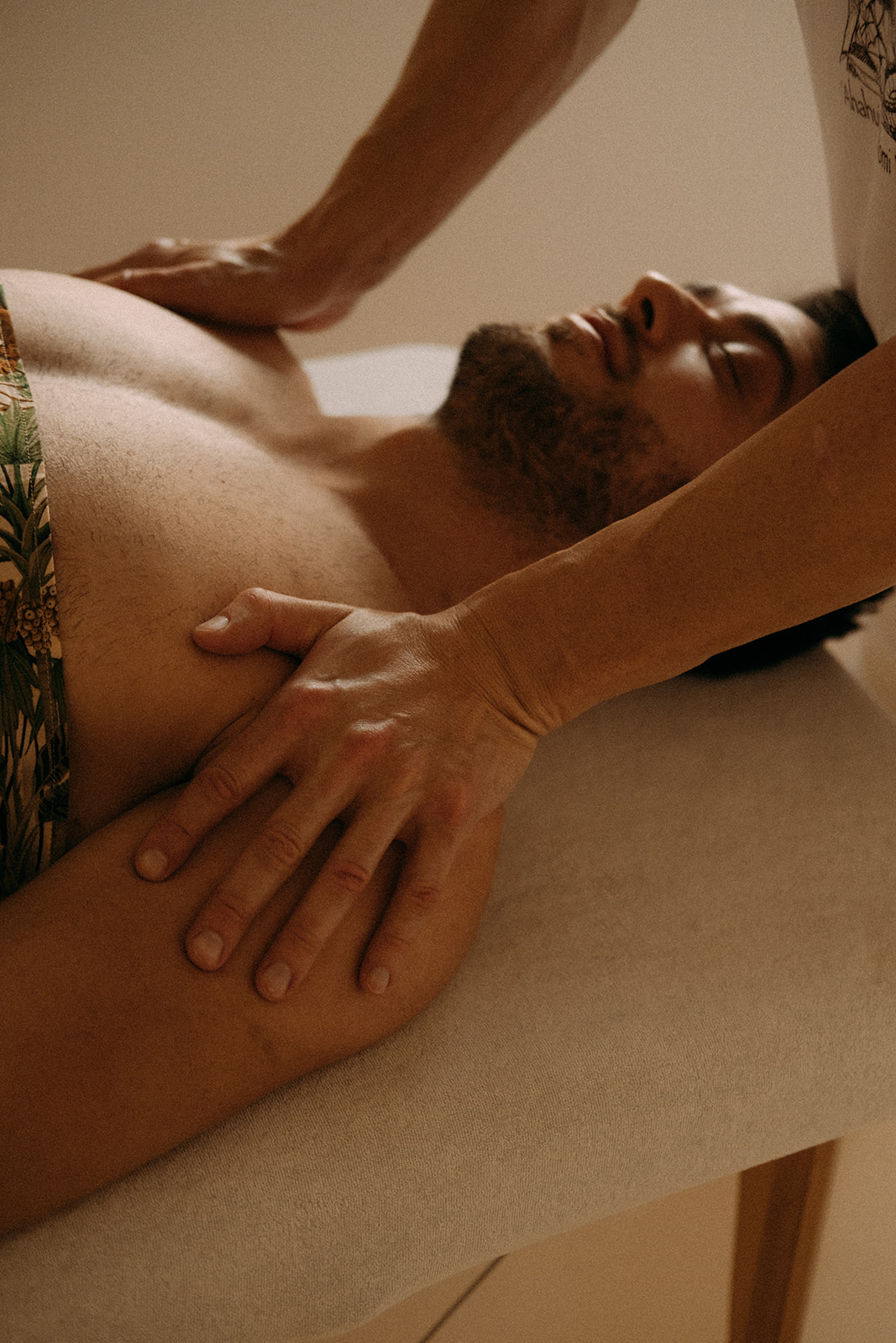 Ein Mann liegt auf dem Rücken auf einer Massageliege. Am Kopfteil der Massageliege steht der Masseur. Er massiert den Mann mit beiden Händen 