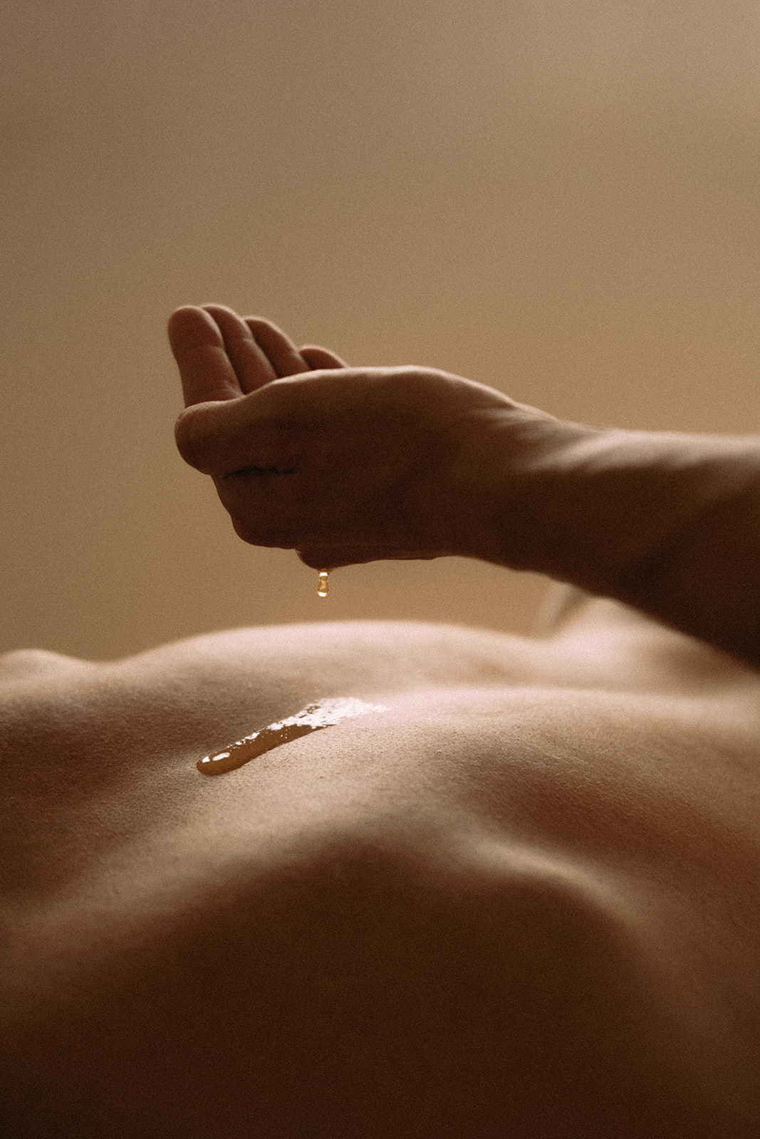 Eine Hand ist gefüllt mit Massageöl. Das Massageöl tropft auf einen Rücken.