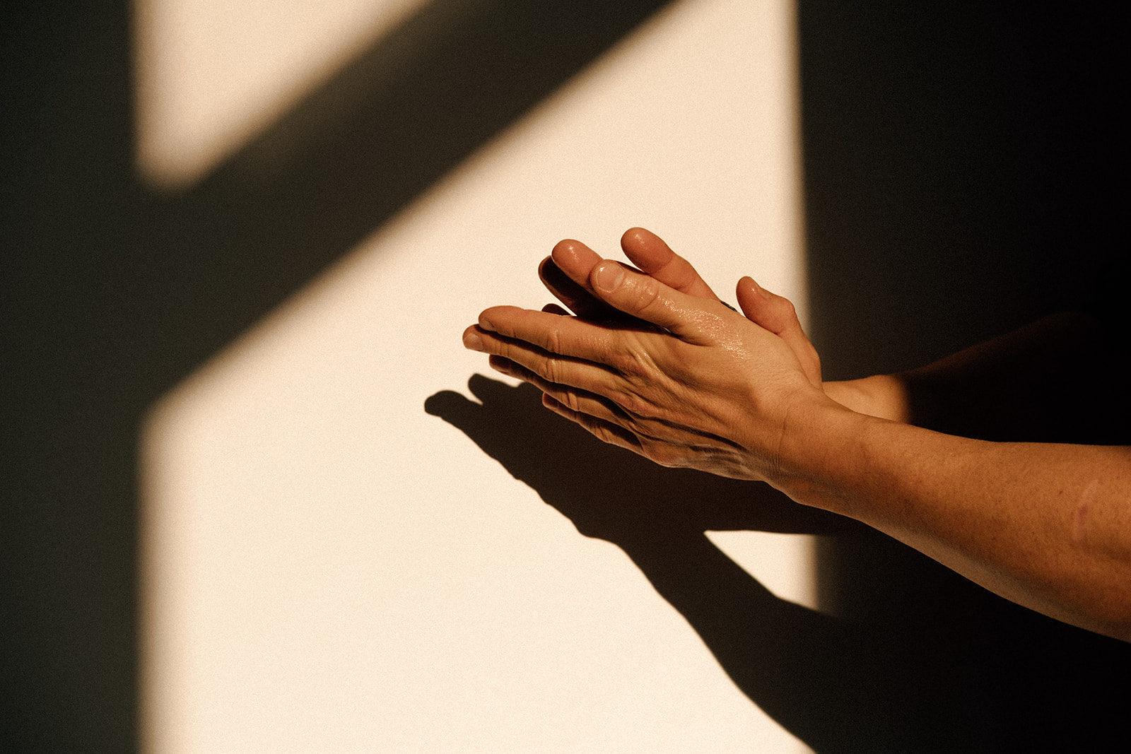 Zwei Hände reiben aneinander. Sie befinden sich vor einer Wand mit Schatten.