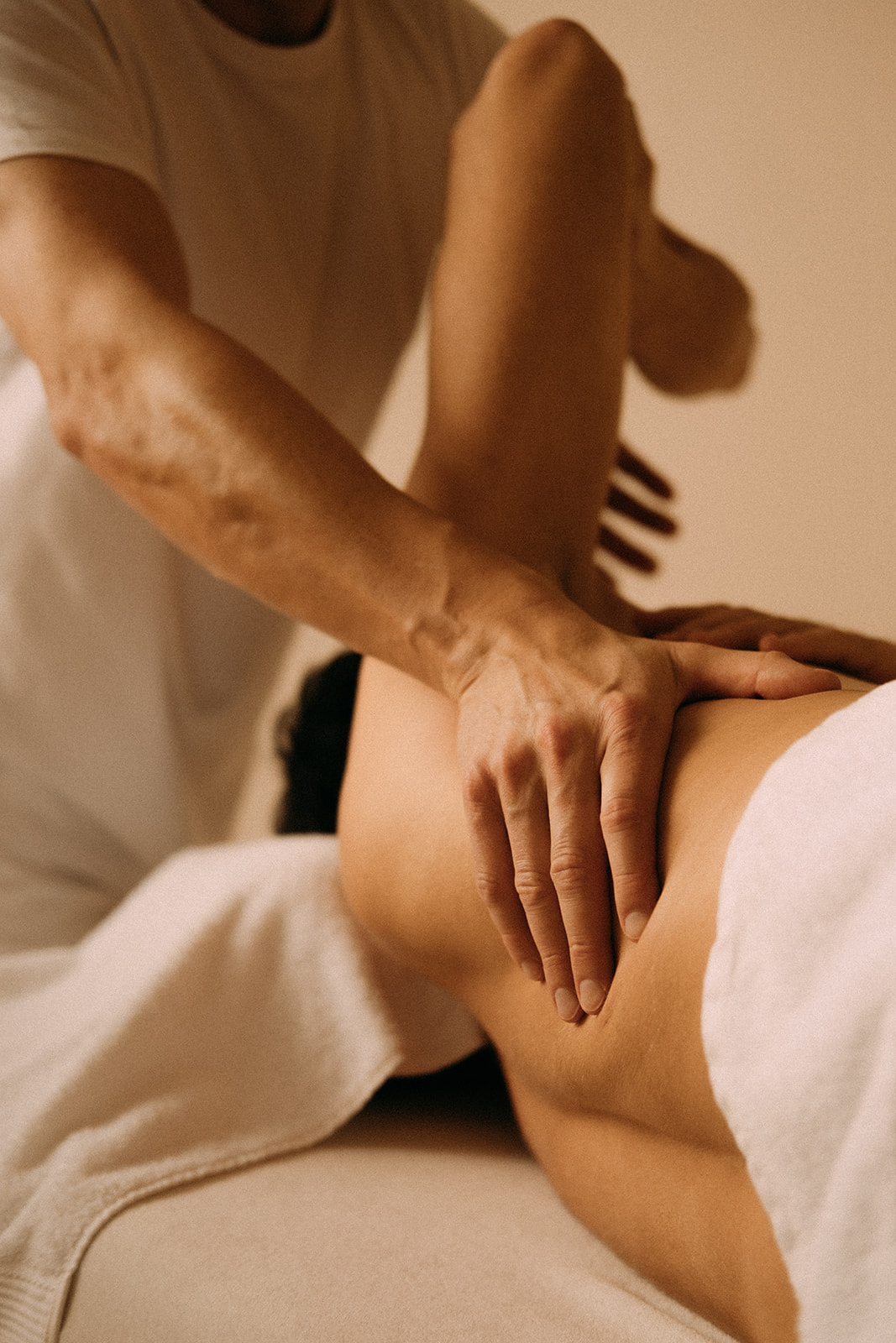 Ein Mann liegt seitlich auf einer Massageliege. Er wird unter dem Arm an den Schulterblättern von einem Masseur massiert.