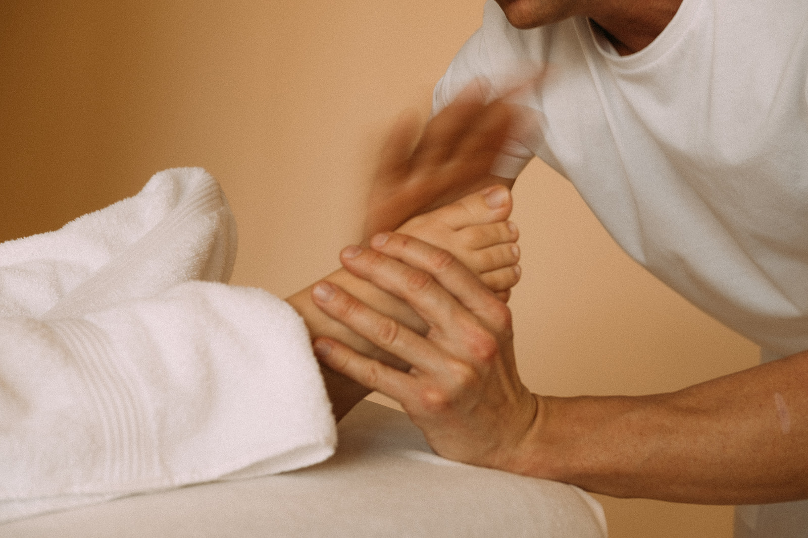 Der Masseur hält mit beiden Händen einen Fuss der Patientin. Die eine Hand massiert mit schnellen Bewegungen die Seite des Fusses.