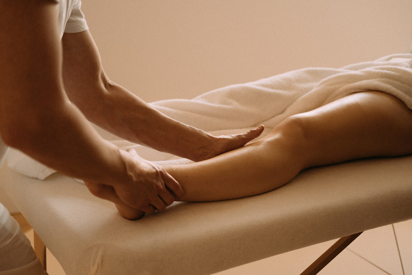 Der Masseur massiert mit einer Hand die Fusskehle. Mit der anderen Hand massiert der Masseur die Wade einer Patientin.