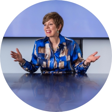 Dr. Victoria Medvec, a middle-aged woman with short brown hair, communicates with her hands at the head of a conference table.