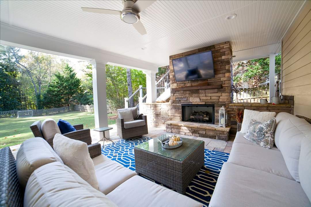 Finished under deck area, a stone fireplace, mounted TV, and a blue patterned rug overlooking a green backyard.