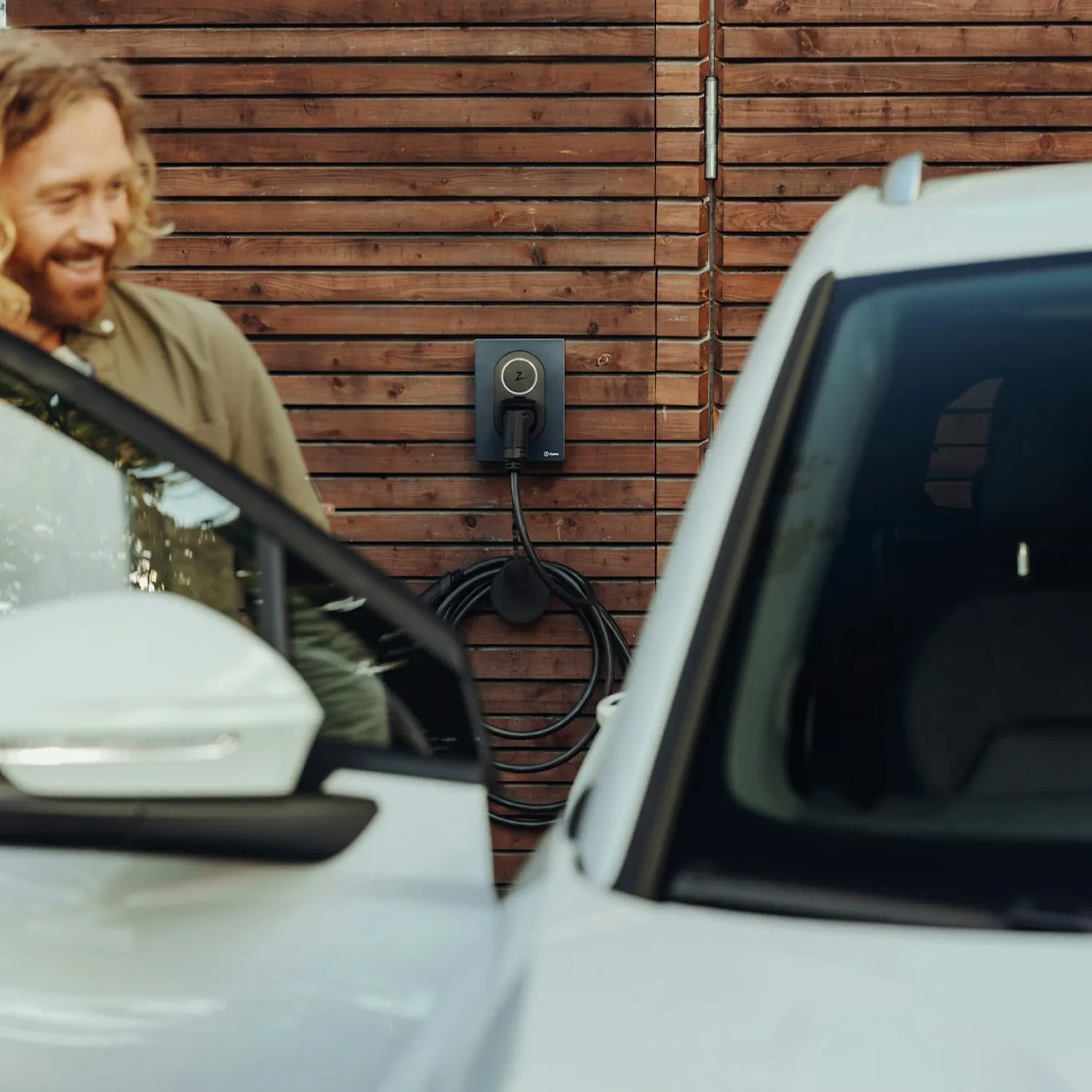Home EV charger mounted on the side of a wall, as a man smiles while getting into his electric vehicle