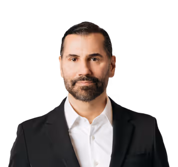 Man with short dark hair and beard wearing a white shirt and black blazer.