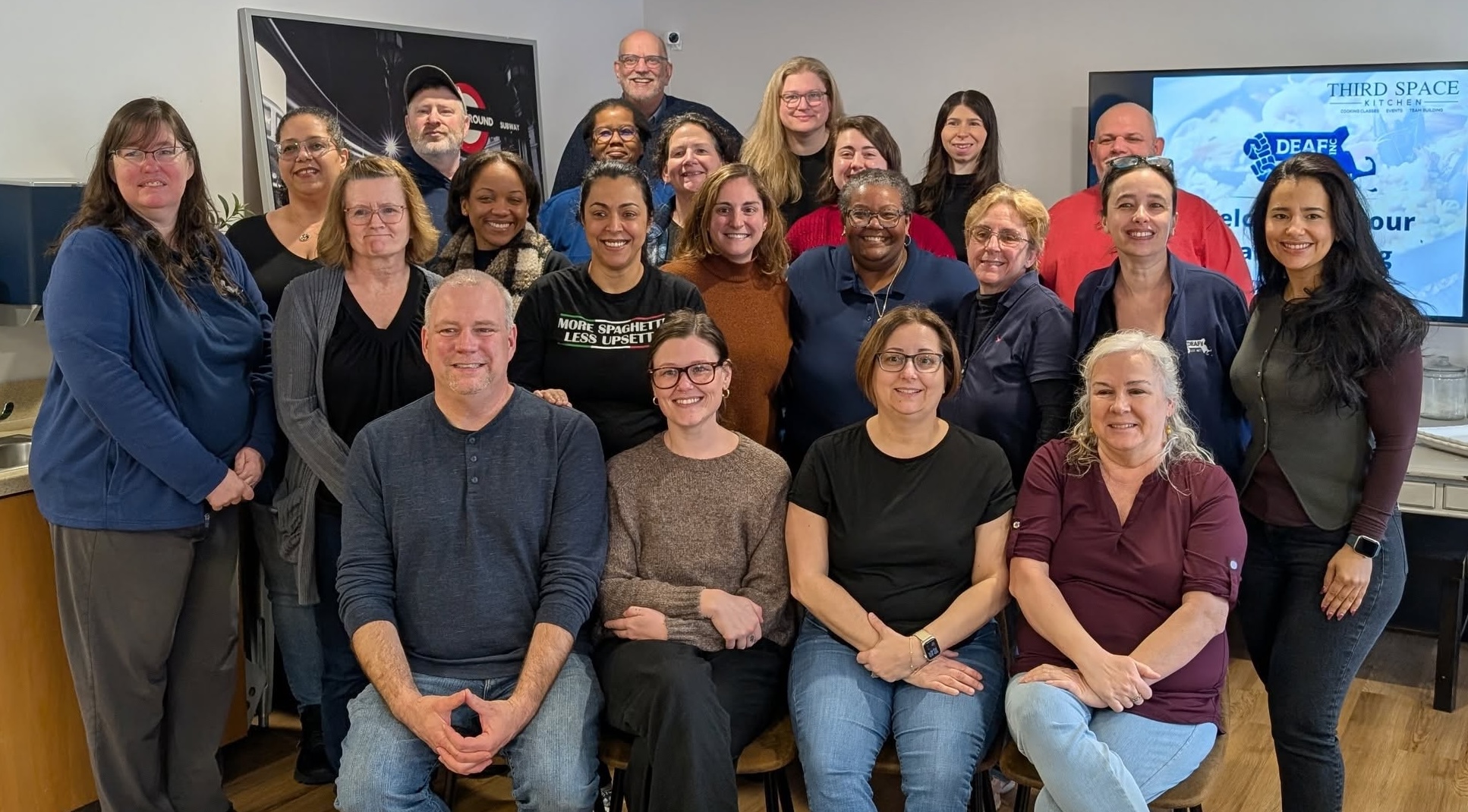 All DEAF, Inc. staff, 4 sitting in front and the rest standing behind, smiling for the camera before the adventure begins!