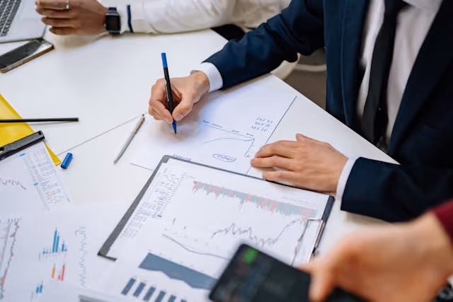 Close-up of business people analyzing financial charts and graphs on paper and writing notes at a desk.
