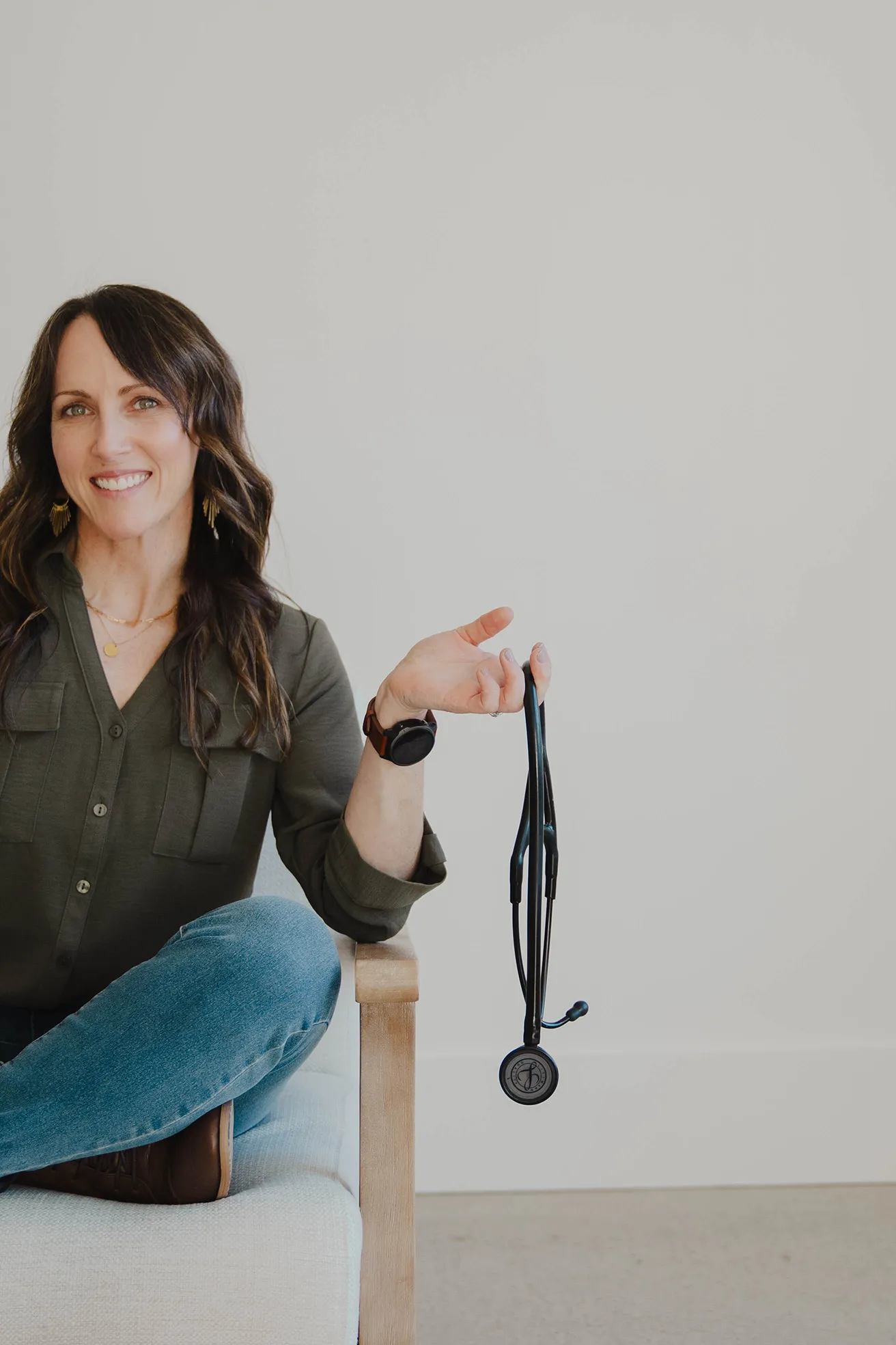 Andrea Giachetti sitting cross-legged in a chair, holding a black stethoscope with one hand.