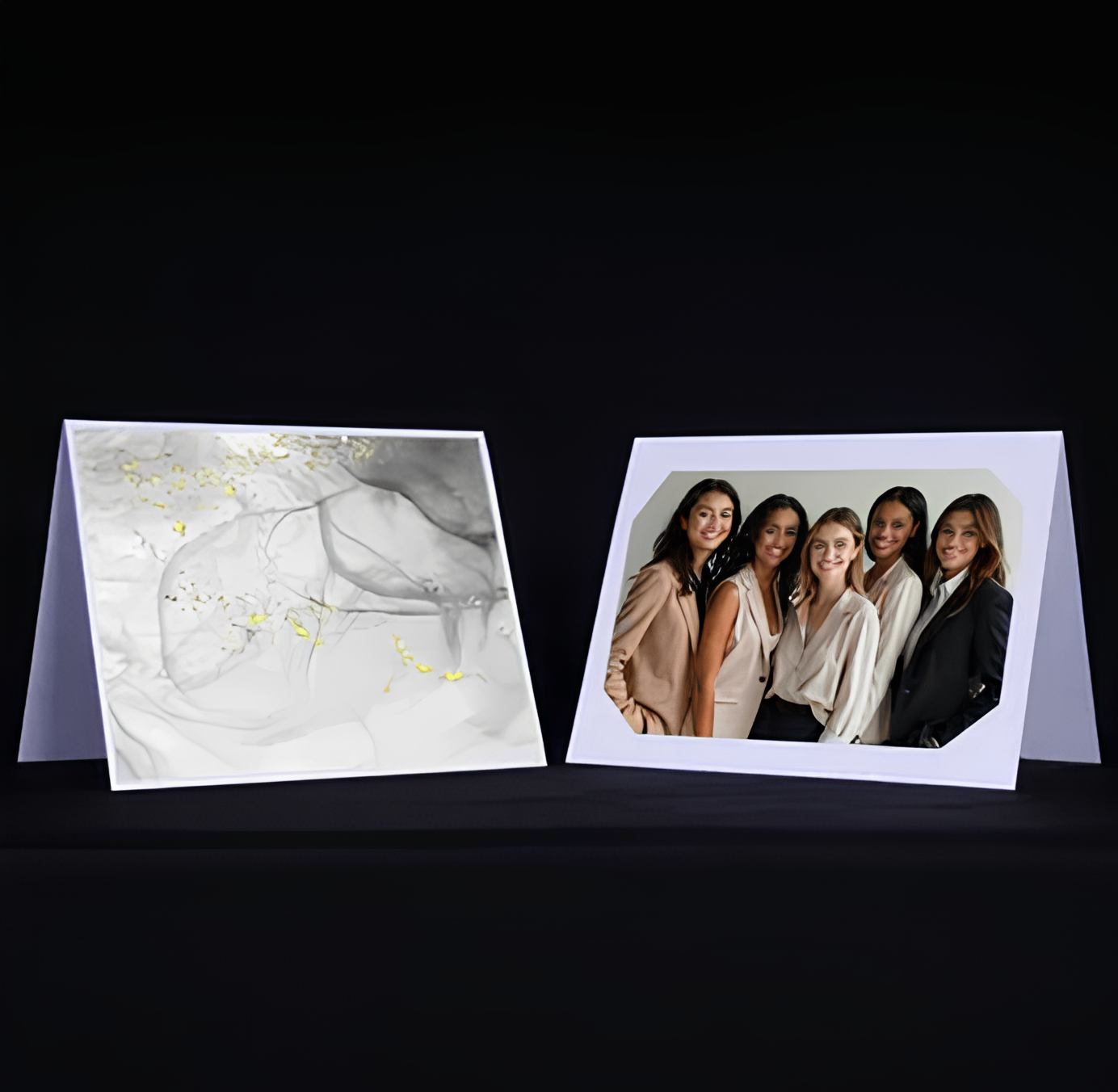 Two folding cards on a black surface; left card with abstract white and gold design, right card featuring five women dressed in neutral and dark business attire.