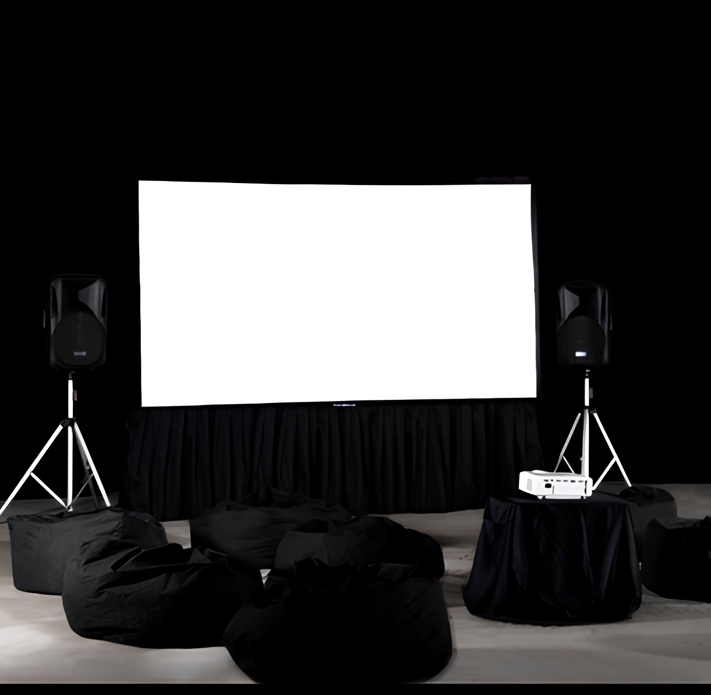Indoor home theater setup with a blank white projector screen, two speakers on stands, a projector on a table, and black bean bag chairs on the floor.