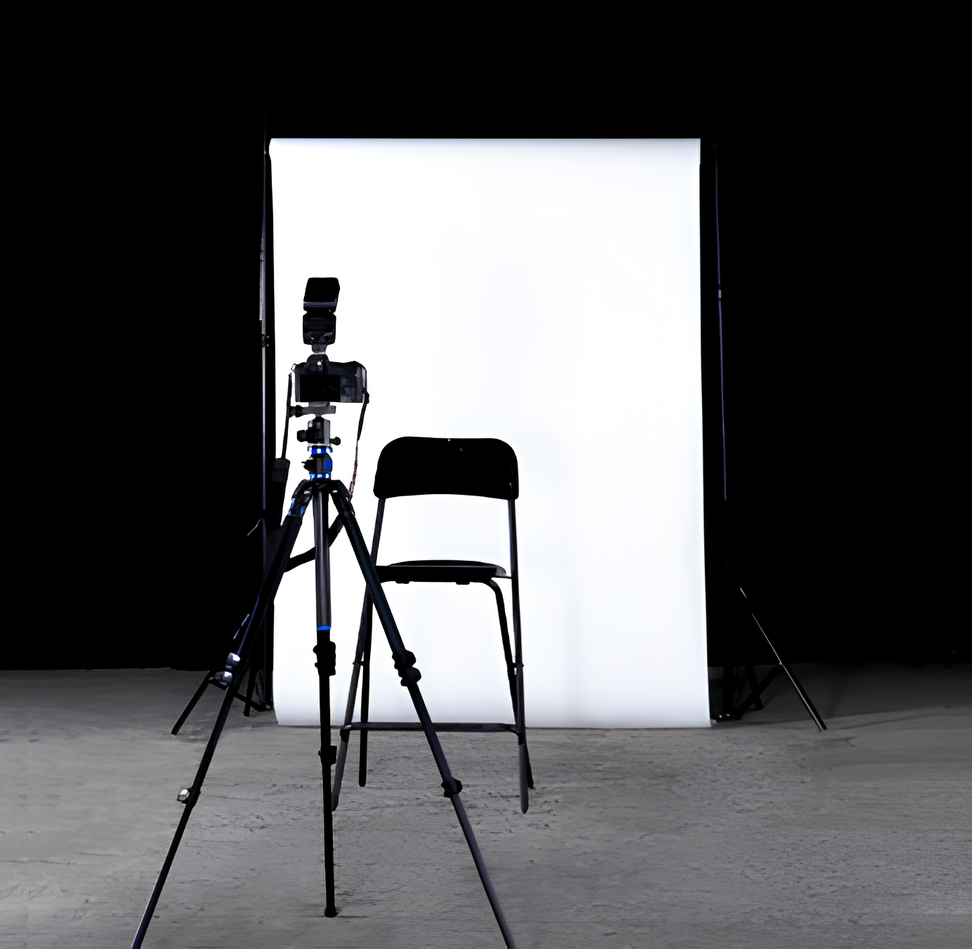 Photography setup with a camera on a tripod and a black folding chair in front of a white backdrop.