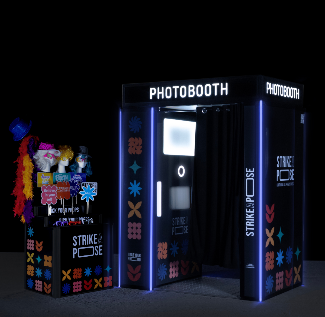 Two women posing for a photo while a third woman holds a ring light and camera, all dressed in black.