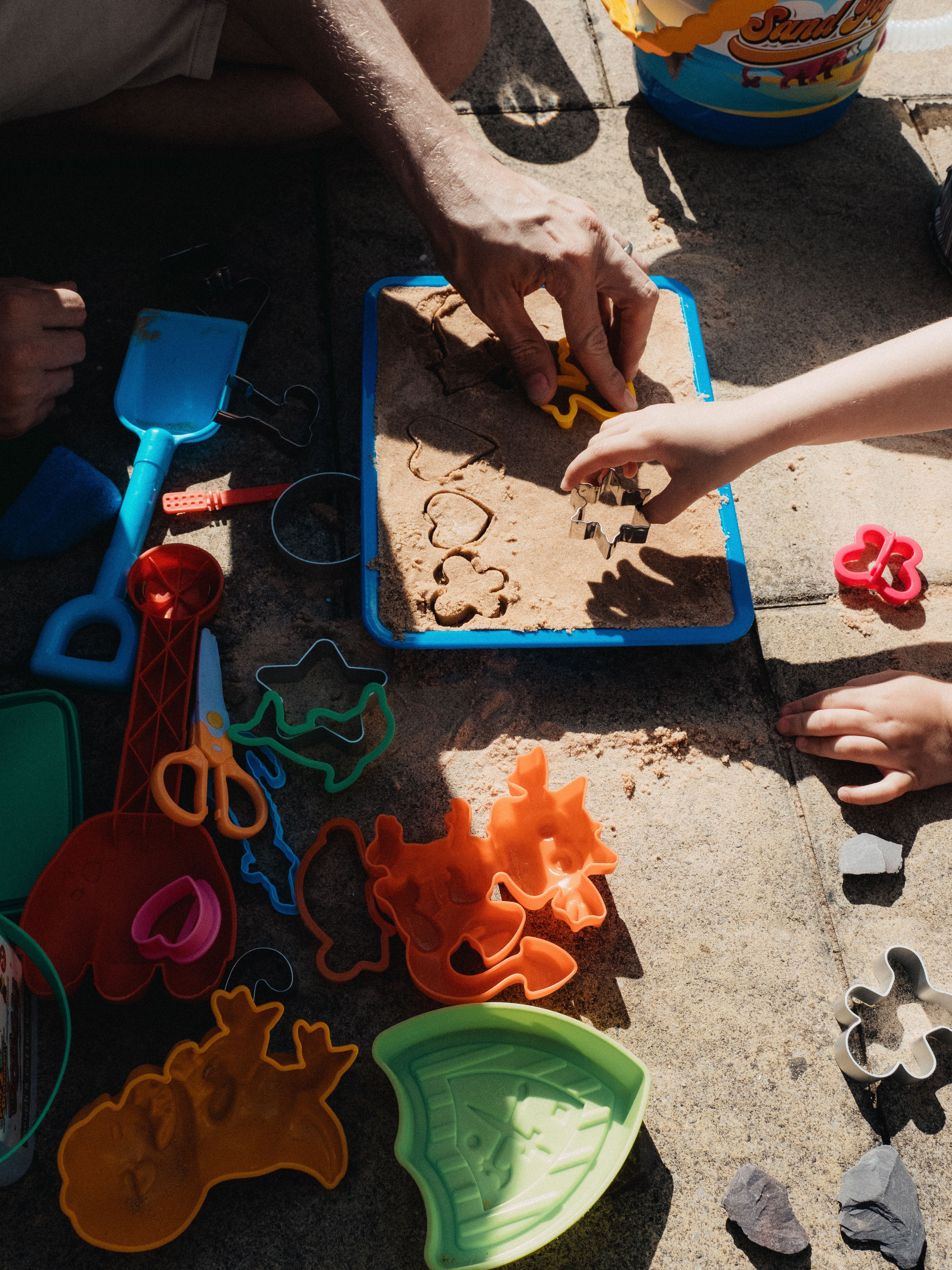 Adult and children shaping sand with molds during an outdoor vacation care activity.