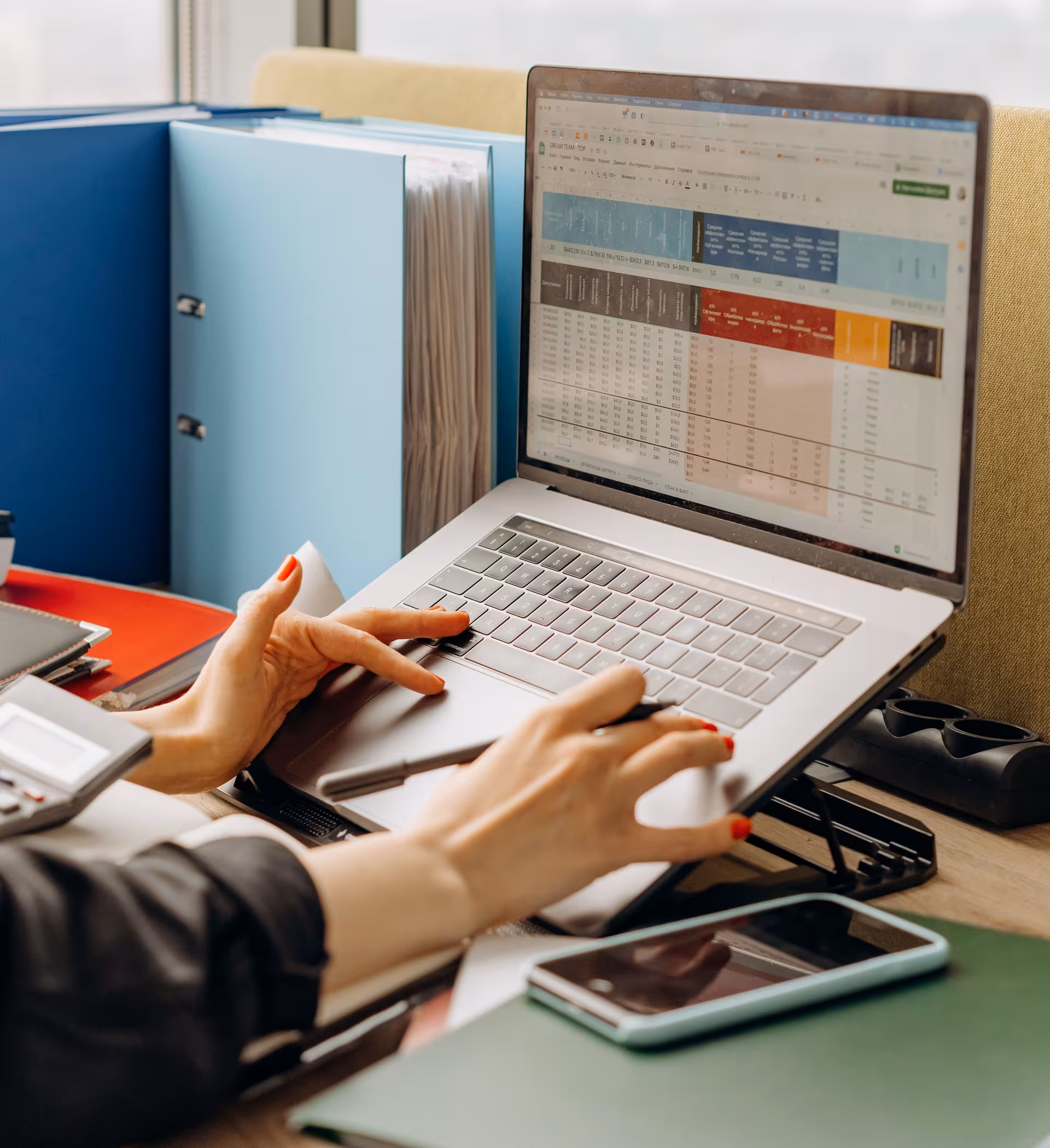 Woman with red nail polish typing on a laptop showing a spreadsheet