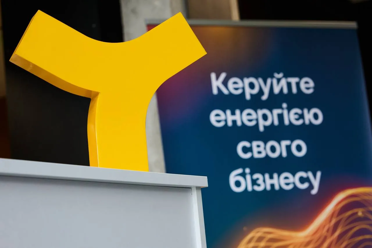 Жовта триспрямована фігура на білому столі на фоні синього банера з текстом українською.