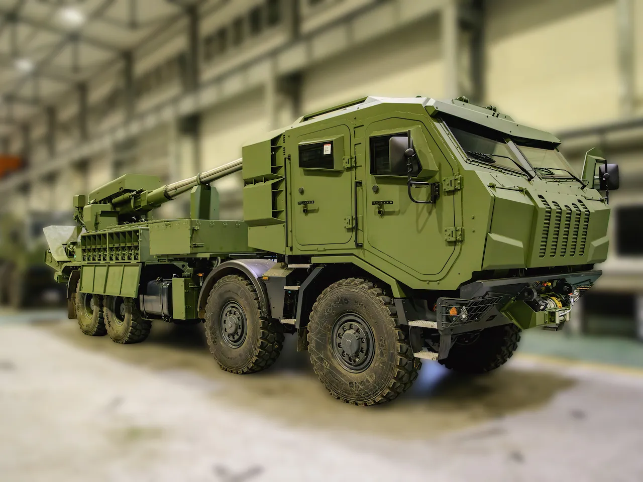 Зелений військовий броньований вантажівка з артилерійською установкою на заводі.