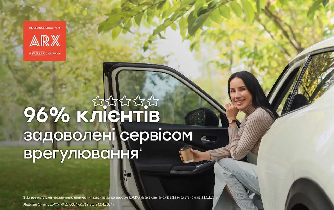 Жінка з темним волоссям посміхається, сидячи в білому автомобілі з відкритими дверима, тримає стакан кави.