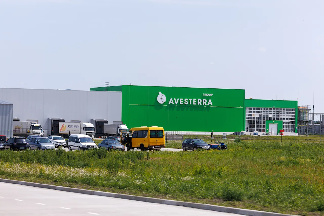 Зелене промислове приміщення AVESTERRA з автомобілями і автобусами на стоянці біля нього.