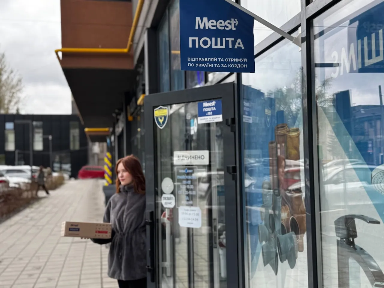 Жінка виходить з поштового відділення Meest з пакунком у руці.
