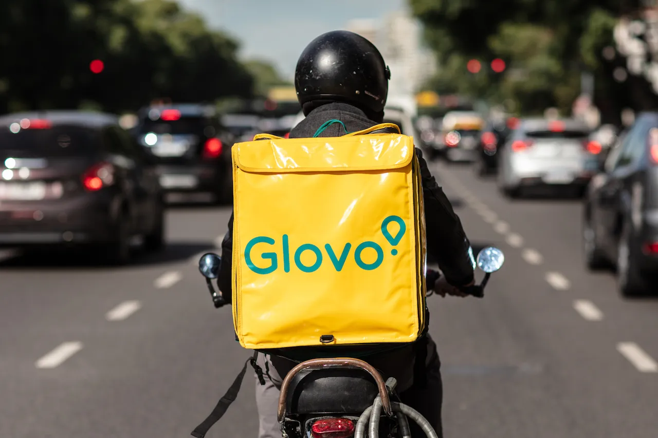 Кур’єри на велосипедах з жовтими рюкзаками Glovo їдуть центральною міською вулицею.