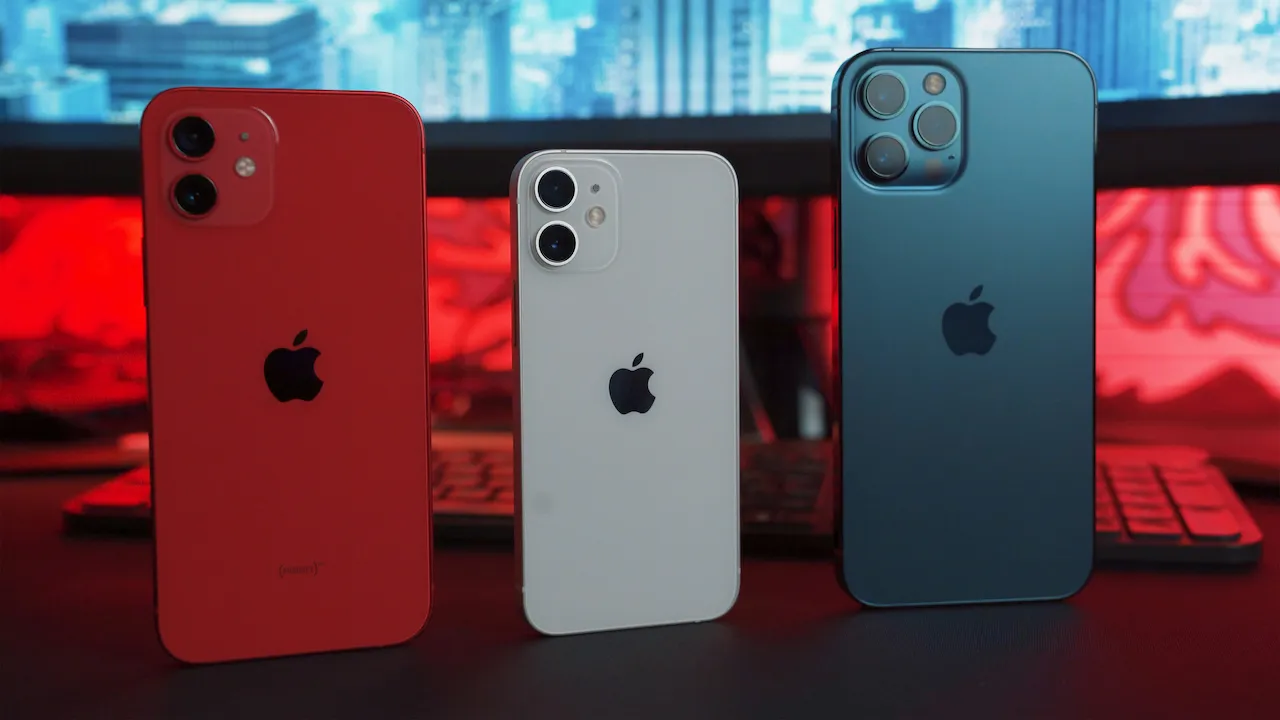 Три iPhone червоного, білого та синього кольорів стоять вертикально на столі.