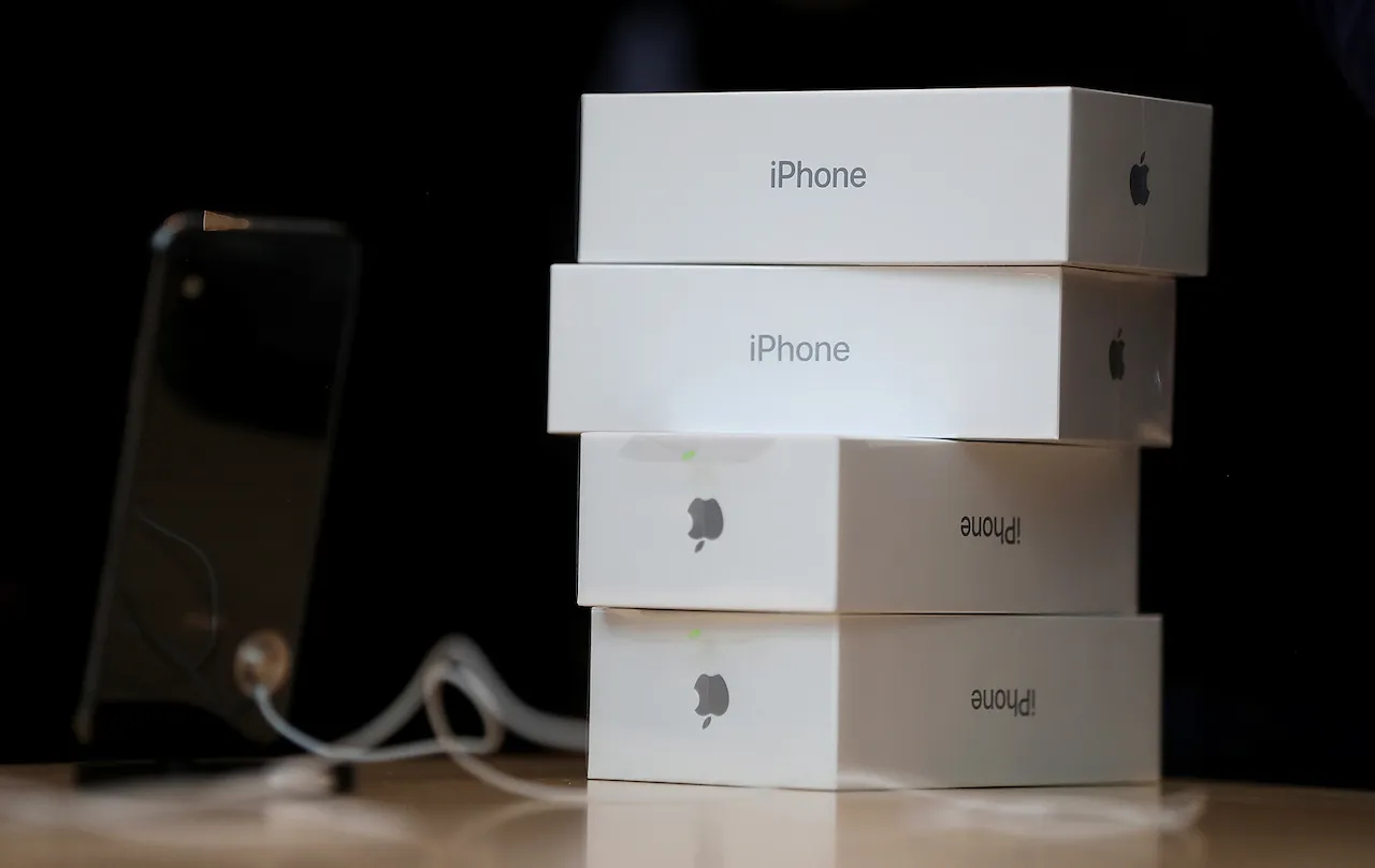 Стопка білих коробок iPhone на столі поруч із підключеним чорним iPhone.