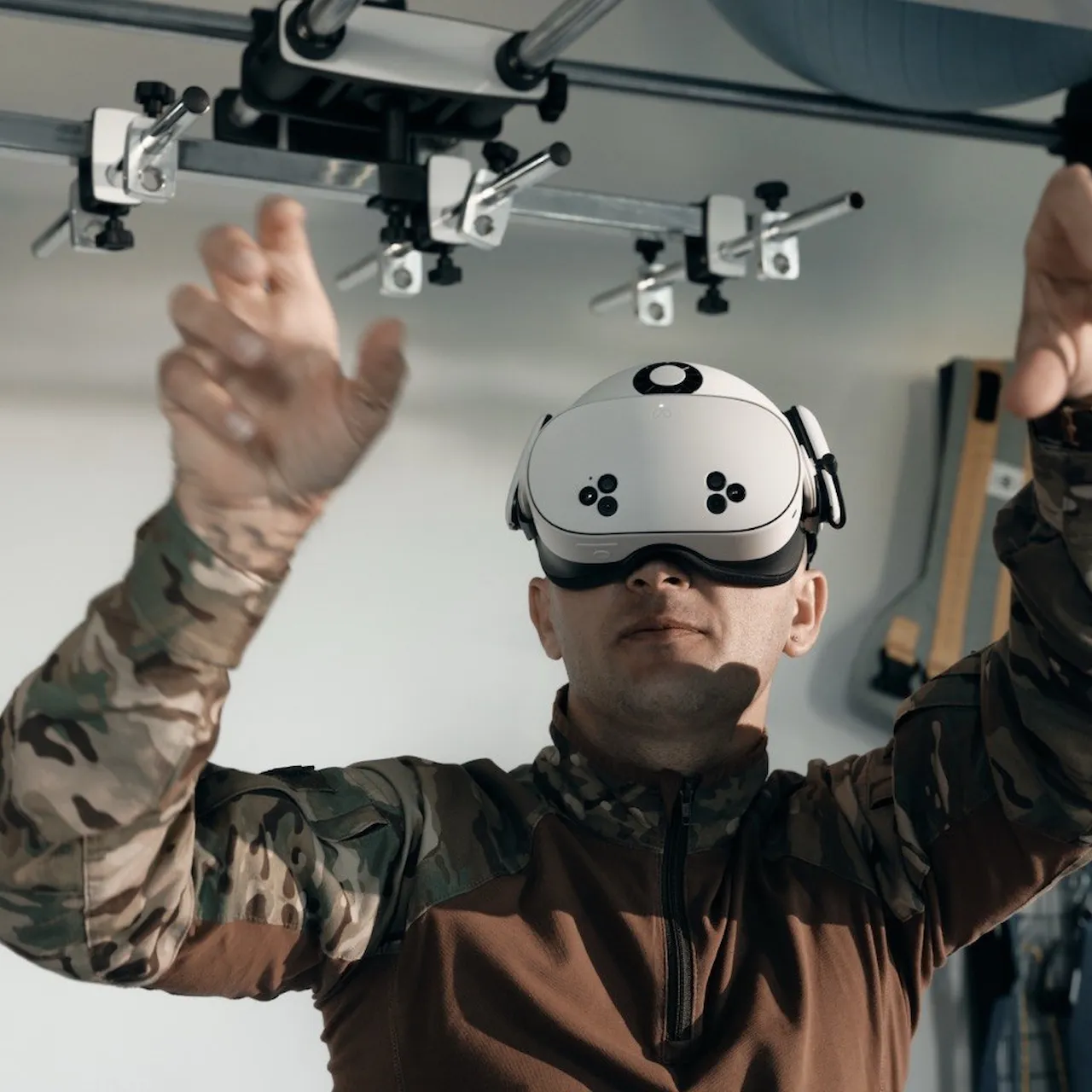 Чоловік у військовій формі, що носить білий VR-гарнітуру і простягає руки вперед, займається віртуальною реальністю у приміщенні.