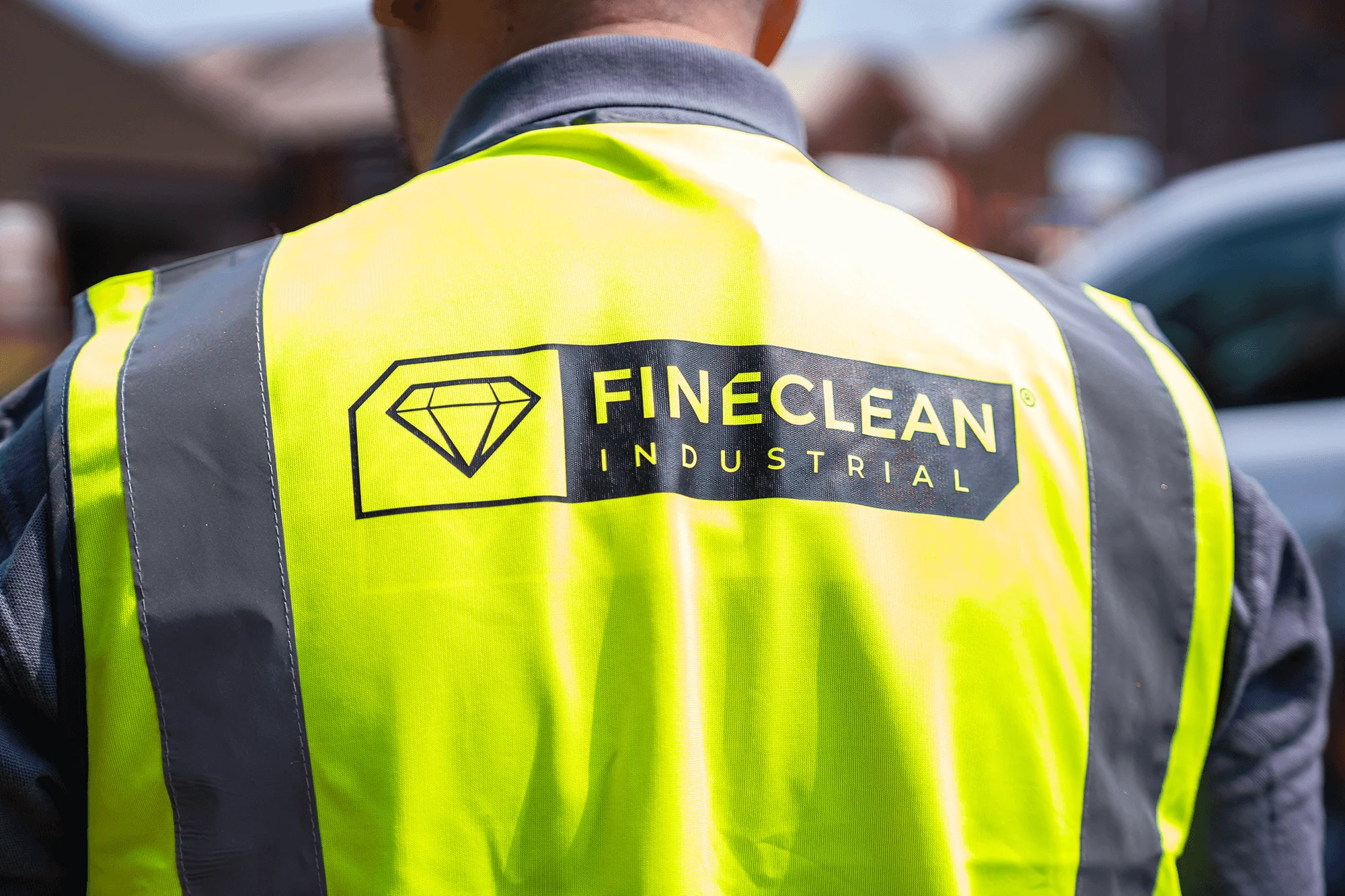 Back view of a person wearing a yellow safety vest with grey reflective stripes and a FineClean Industrial logo.