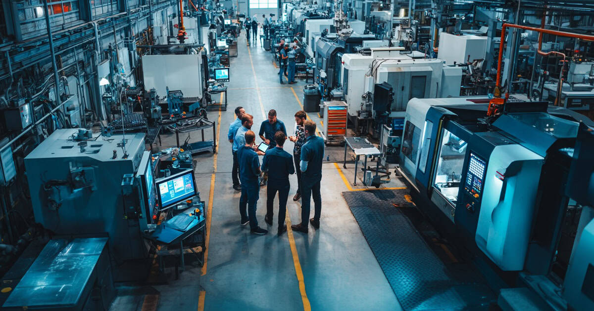 Manufacturing engineers collaborating on the production floor while reviewing digital equipment data.
