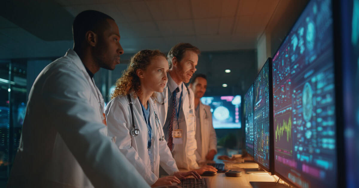 Healthcare professionals working with an IT specialist to monitor and support clinical technology systems.