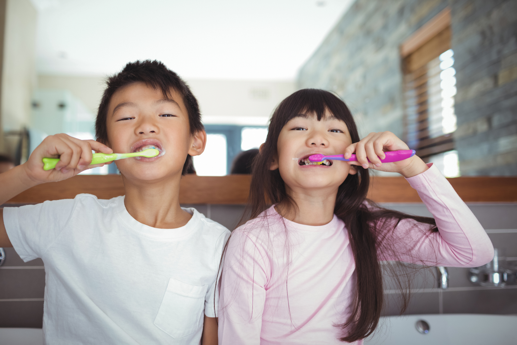 Two young siblings brushing their teeth together at the bathroom sink