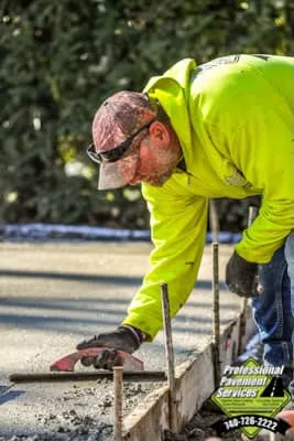 A construction worker wearing a neon yellow jacket and a cap is carefully troweling concrete along a form.